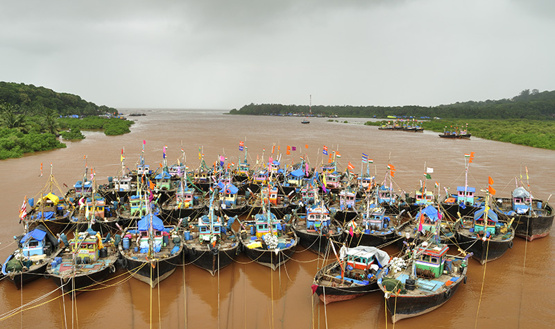Many south Asian fishing boats grouped together on reddish brown water.
