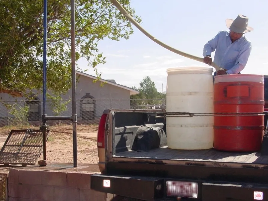 photo of a person using a pickup truck to bring tanks of water to a home on the Navajo Nation in Arizona