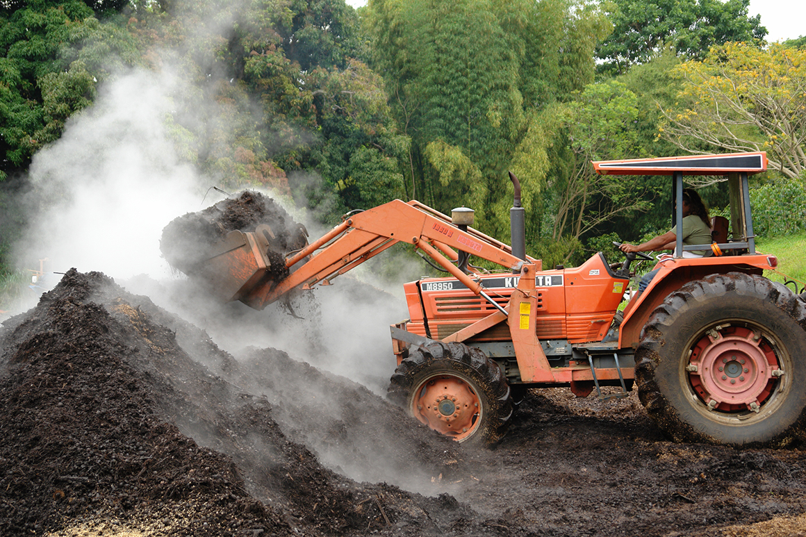 This is a photo of a tractor moving a pile of steaming compost.