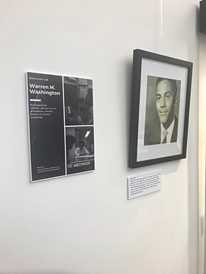 Sign with exhibit title and description next to framed photograph of Warren Washington as a college student.
