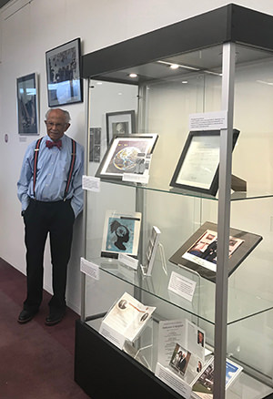Dr. Washington with the Exhibit. Warren Washington stands next to the exhibit display case, 2019.