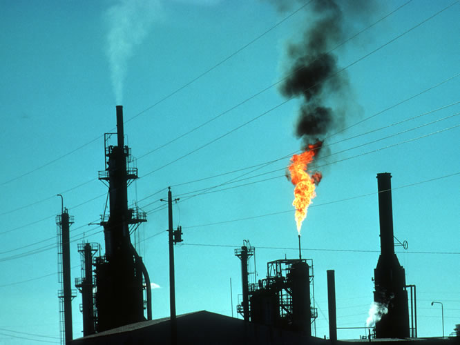 Multiple smokestacks releasing pollutants into the air in the form of white smoke, burning natural gas, and black smoke.