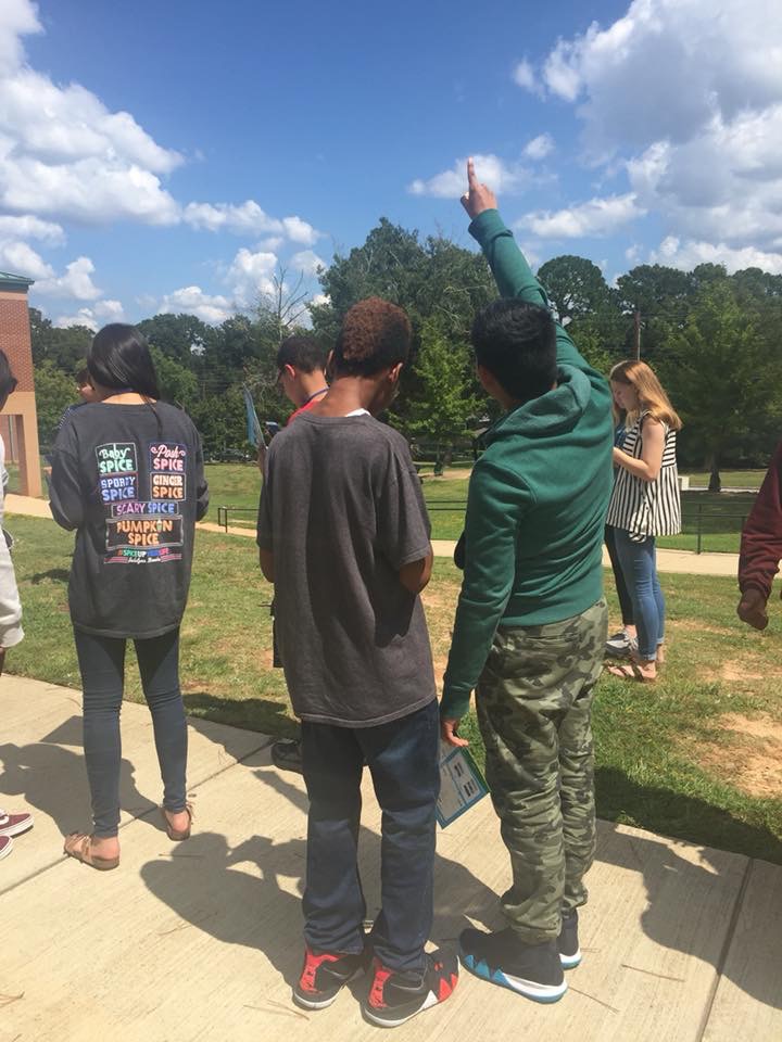 Students are outside observing clouds and conditions in the sky. One student points upwards at something in the sky.