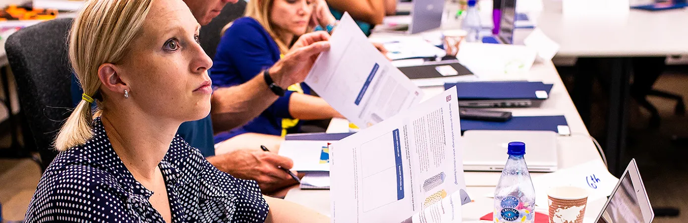 Teachers sitting at a table with laptops and papers in front of them are engaged in a learning experience.