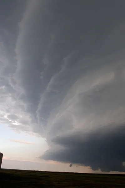 A large, dark storm cloud rises high up into the sky above a dark horizon.