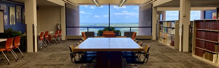 Several tables and chairs in the library with artwork on the left side and books lining the right side.