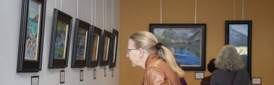 A few people looking at framed and labeled art on the walls in the Mesa Lab Café. 