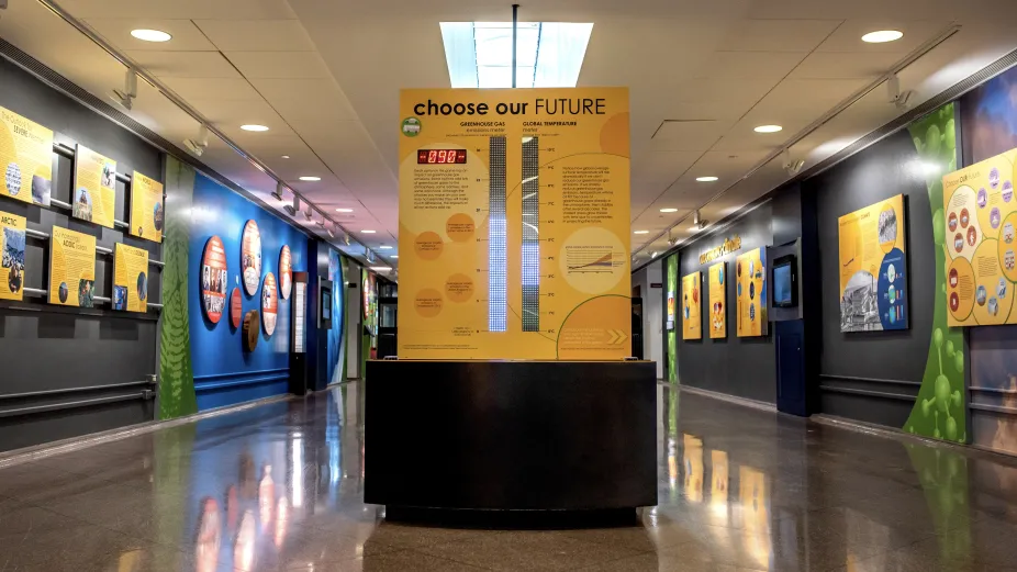 A view of the climate exhibit that shows the "Choose Your Future" interactive with exhibit signs along the walls on both the left and right sides.
