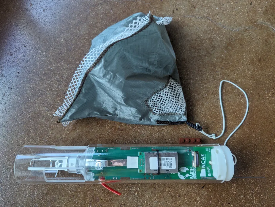 photo of a dropsonde instrument including a sensor for measuring atmospheric pressure and winds, and a parachute for slowing its fall through the air