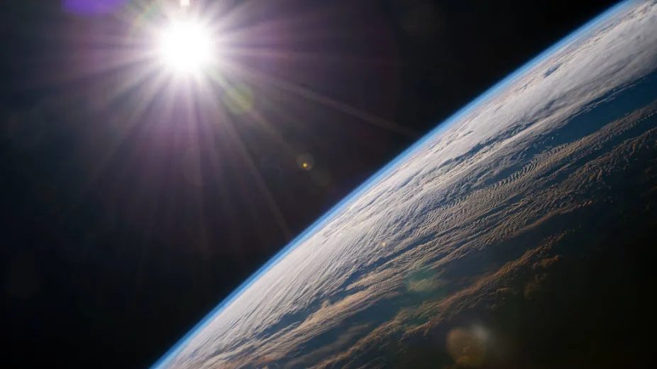 The bright Sun shines through space above the Earth.