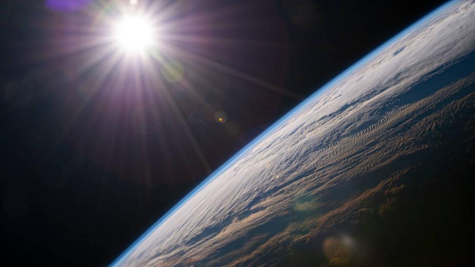 The bright Sun shines through space above the Earth.
