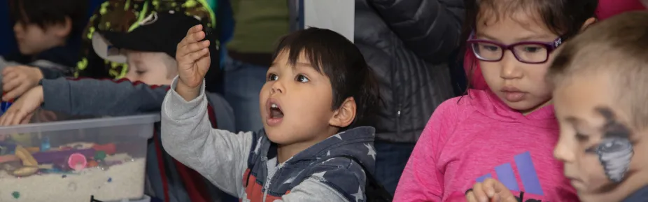 A student gazing wondrously at a small object they are holding in their hand. Around this student are other students interacting with similar small objects.