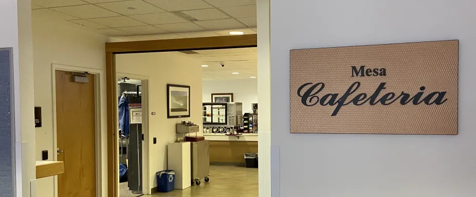 A photo of the entrance to the NCAR Mesa Lab Café which has a sign that reads “Mesa Cafeteria.” In the background you can see a lunch tray station part of the Café itself.