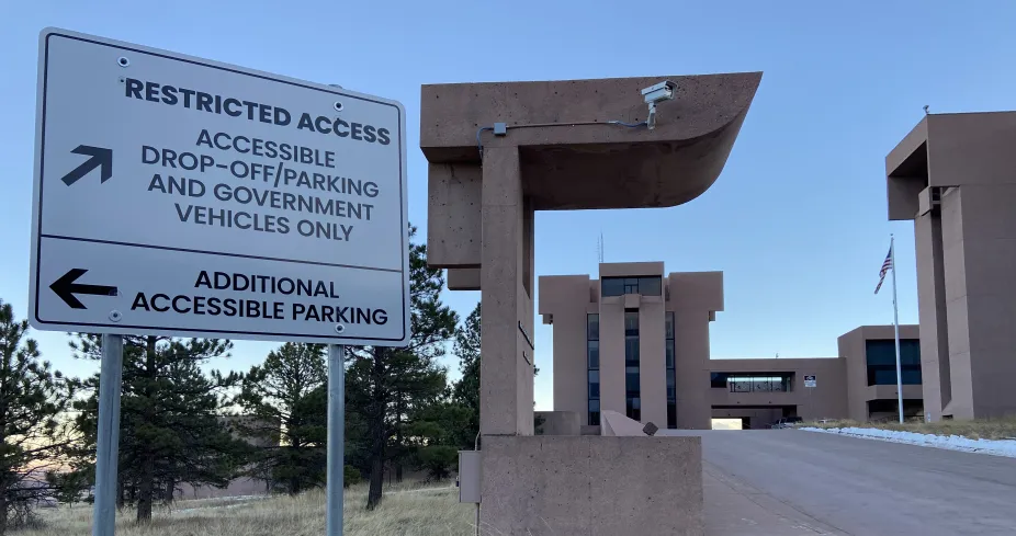 A photo of the sign in front of the ramped driveway up to the Mesa Lab. One section reads “Restricted Access: accessible drop-off/parking and government vehicles only” with an arrow pointing up the ramp. The other section shows another arrow pointing down to the main parking lot that reads “Additional Accessible Parking”. 