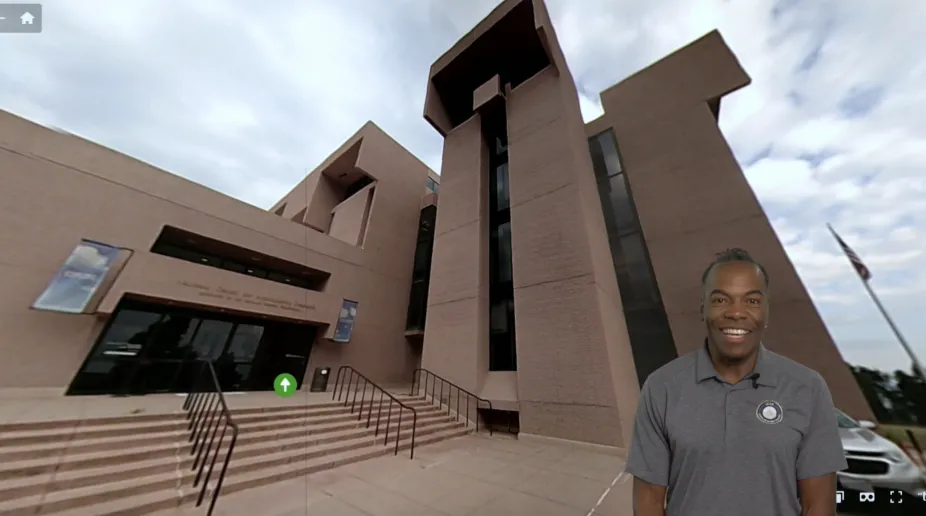 a tour guide stands in front of a digital image of the Mesa Laboratory