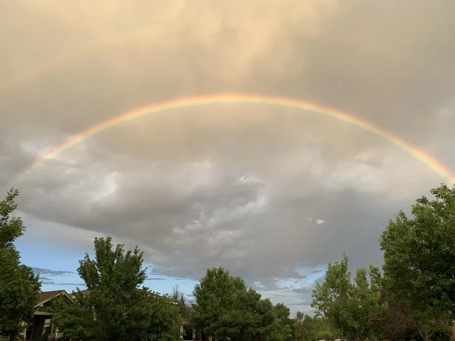 Double rainbow in a sky with clouds overhead and trees down below