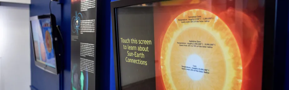 Two touchscreens within the Sun-Earth Connections Exhibit and an exhibit sign in between them.