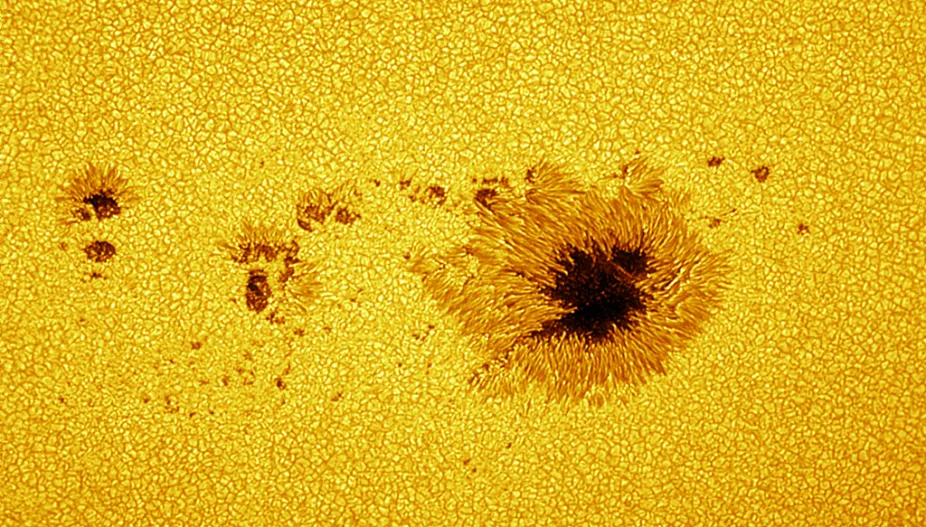 High resolution image of granulation on the surface of the Sun and a dark, irregularly shaped sunspot.