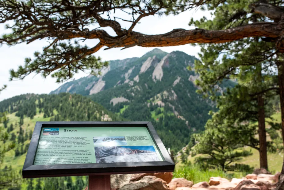 The sign about snow on the weather trail with the flatiron mountains in the background.
