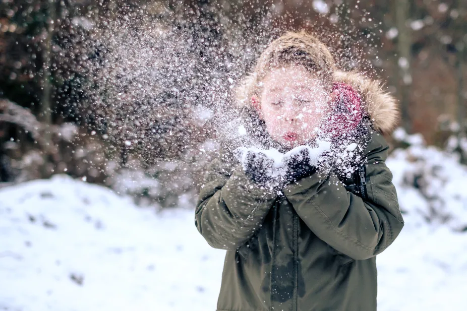 A kid blows on snow that's cupped in their hands and it flies into the air.