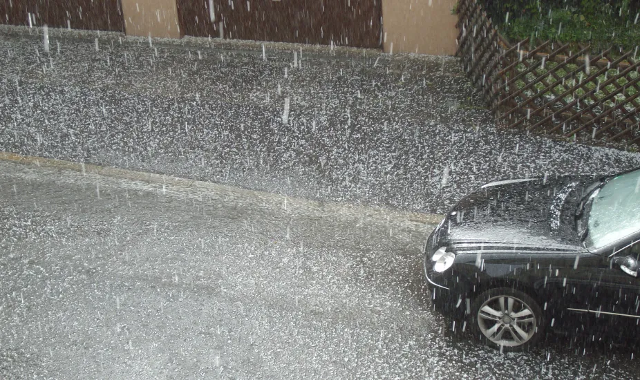 Small hail falling from the sky and onto a street with a car in the lower right on the photo