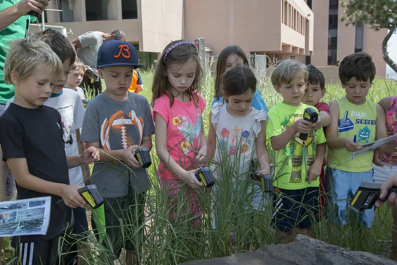 Children stand in tall grass and measure temperature with IRTs.