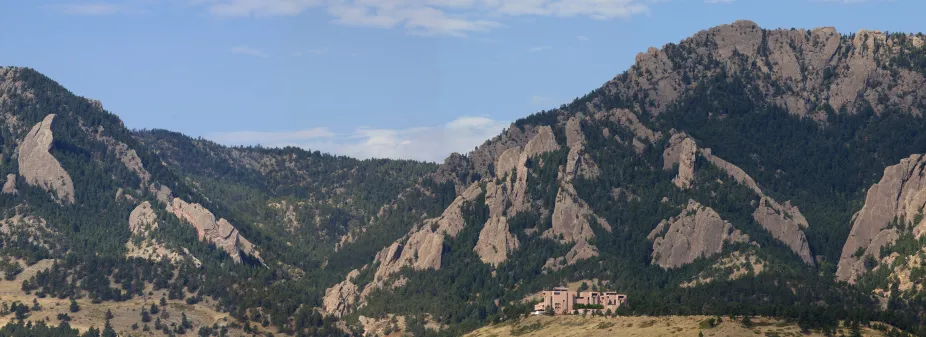 A panoramic photo of the NCAR Mesa Lab showing the Flatiron mountains and a blue sky behind the building.
