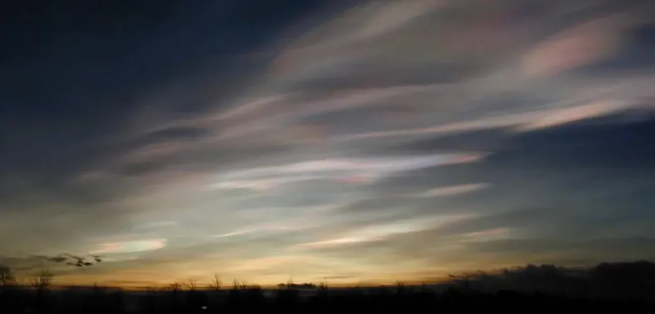 In this photo, the Sun is low on the horizon, and polar stratospheric clouds cover the sky with shimmering, iridescent colors. 
