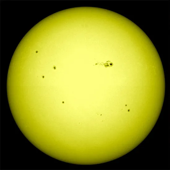 The yellow surface of the Sun with numerous clusters of sunspots.