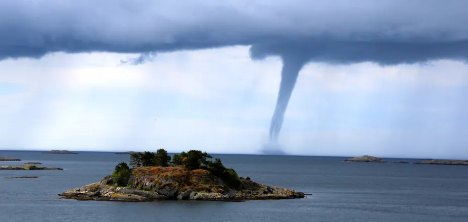 Ocean water with a small island in the foreground and a waterspout in the background