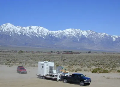 Photograph of a pickup truck with trailer and equipment and snow-capped mountains in background
