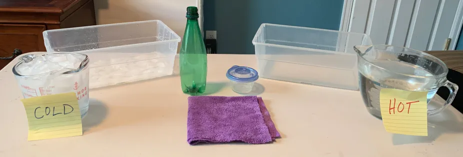 Two rectangular plastic bins, labeled containers of hot and cold water, a green bottle, a purple towel and a small round plastic container