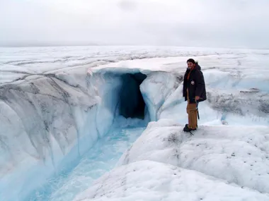 A researcher stands next to a chute in an ice sheet, also called a moulin