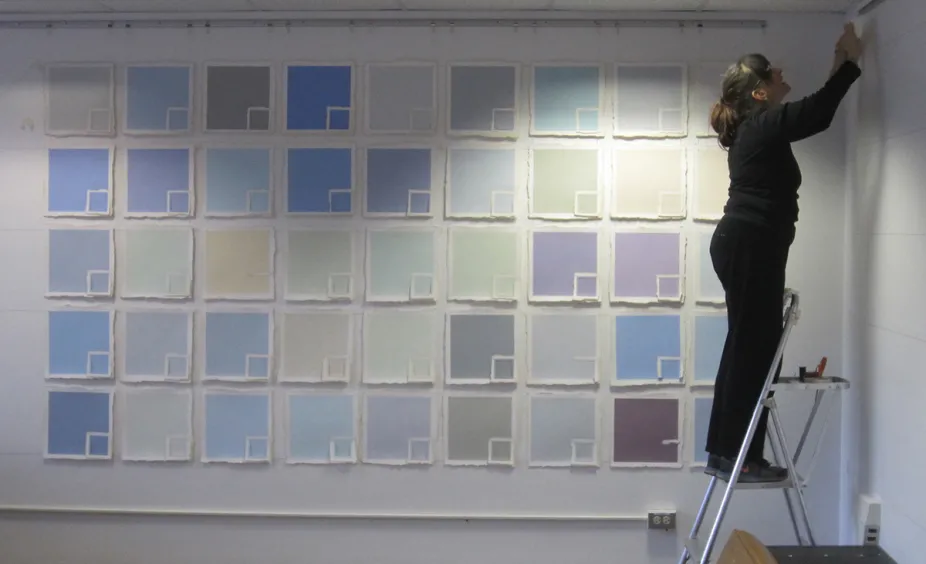 Wall filled with square paper of a variety of colors ranging from blue, to yellow, to brown.