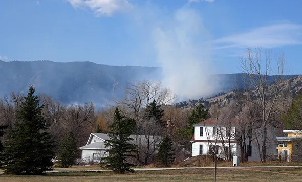 A plume of smoke is rising behind a row of houses from a wildfire in the foothills.