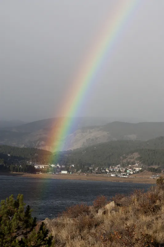 A photo of a rainbow in a misty sky over a small mountain town.