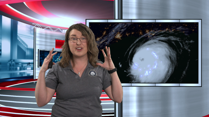 An educator standing in front of a green screen that is displaying a large swirling hurricane.