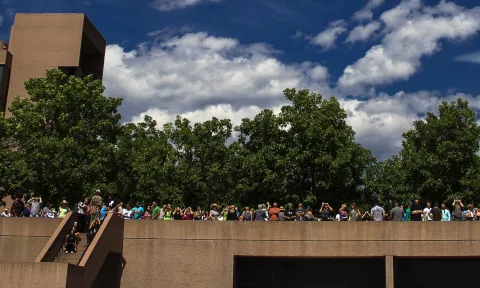 A photo of a row of people on the NCAR Mesa Lab Tree Plaza viewing the solar eclipse using protective eyewear.