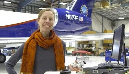A photo of a scientist smiling at the camera with a large research aircraft behind her.
