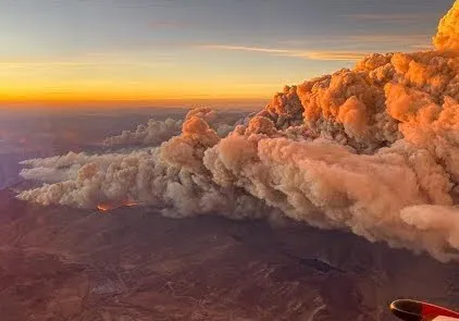 An aerial photo of a wildfire in a mountain range with smoke billowing up.