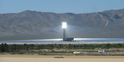 This is an image of a concentrated solar power plant that has a sunlight collection tower against a mountain backdrop. 