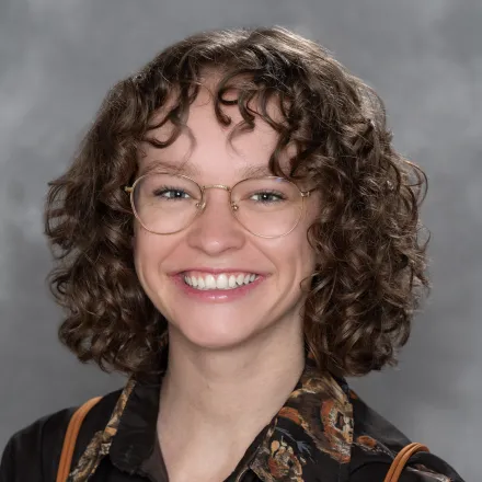 A white woman with curly brown hair and gold rimmed glasses.